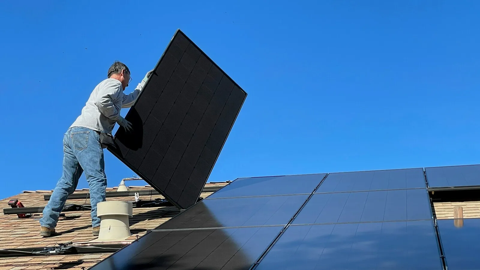 An installer lifting a solar panel into place on a roof