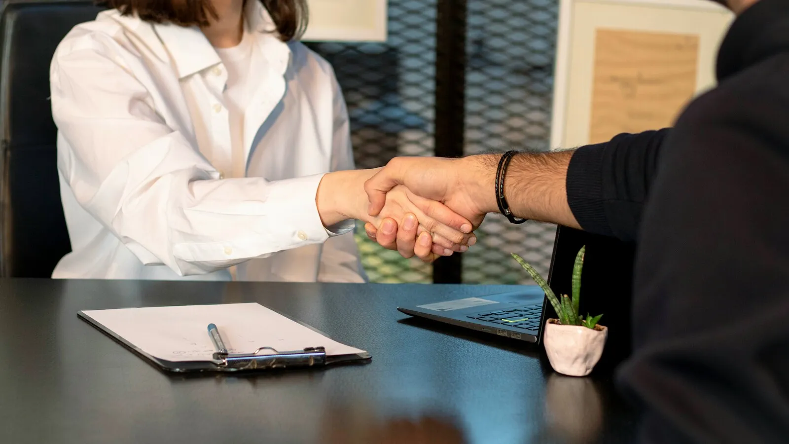 Two people shaking hands over a desk during a meeting